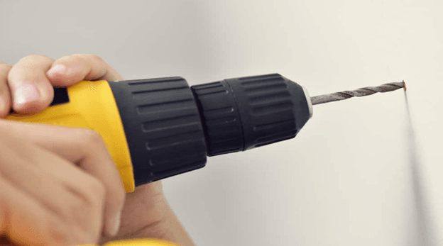 Hand using electric drill machine to drill a hole in wall